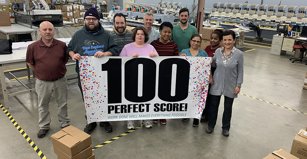 Employees standing behind a banner that read 100 PERFECT SCORE