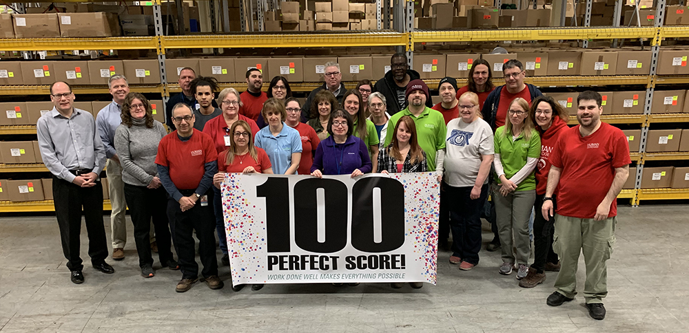 Employees standing behind a banner that read 100 PERFECT SCORE