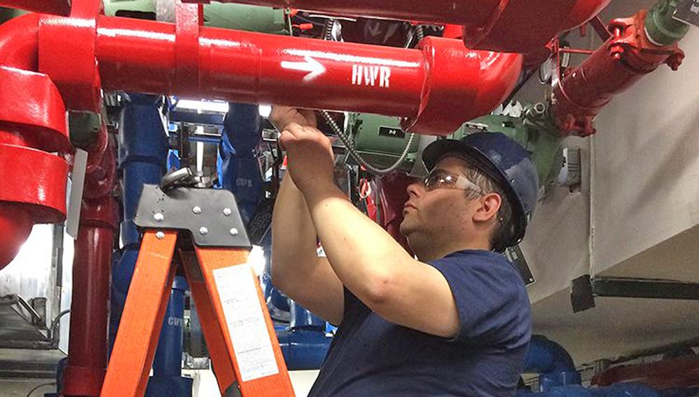 HT employee on a ladder inspecting a pipe